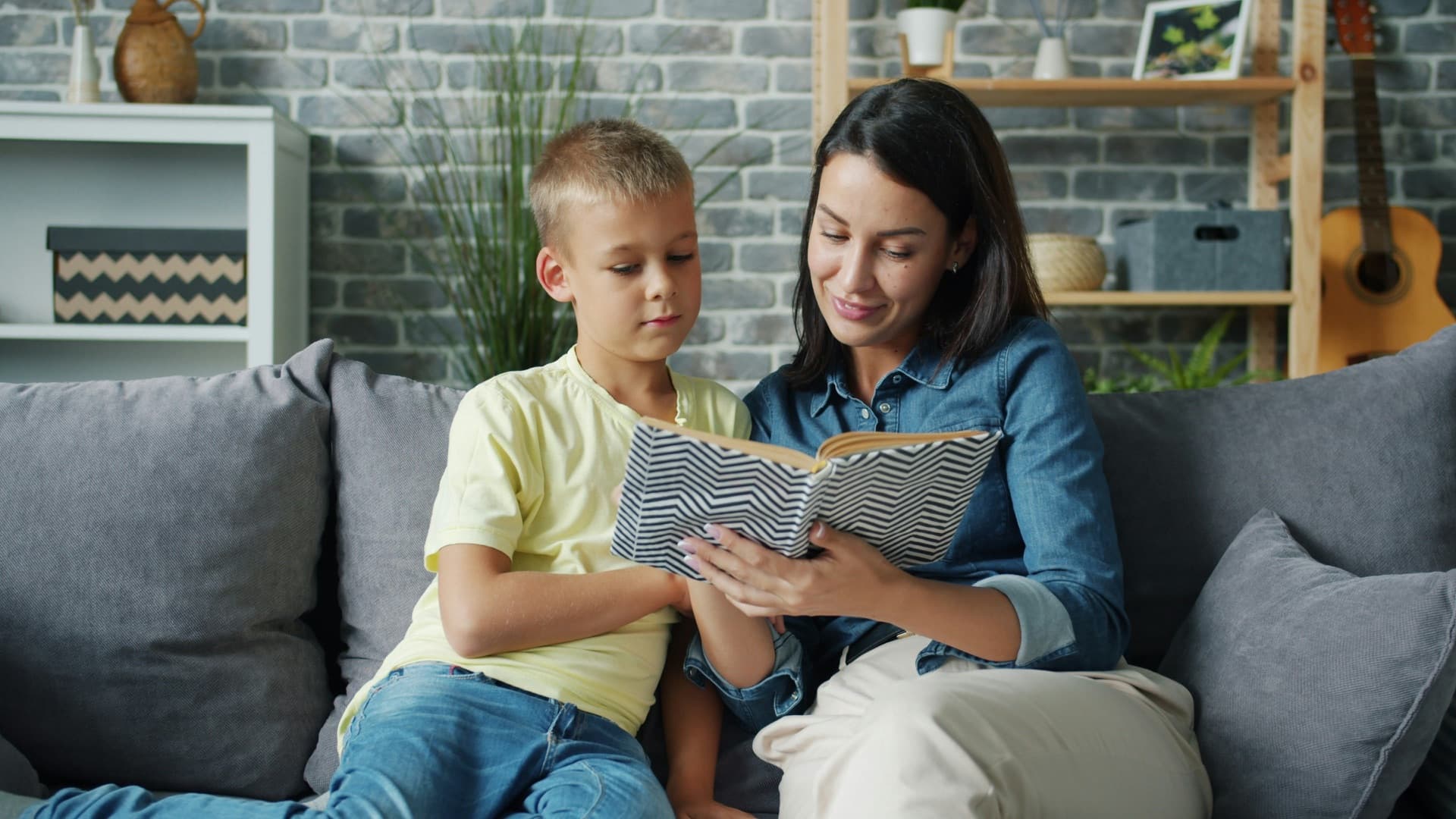 A parent reading a book with a child on a sofa